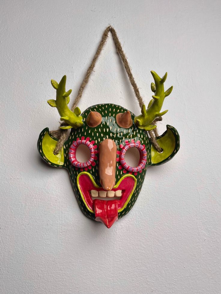 a mask hanging on the wall with green and red decorations around it's eyes