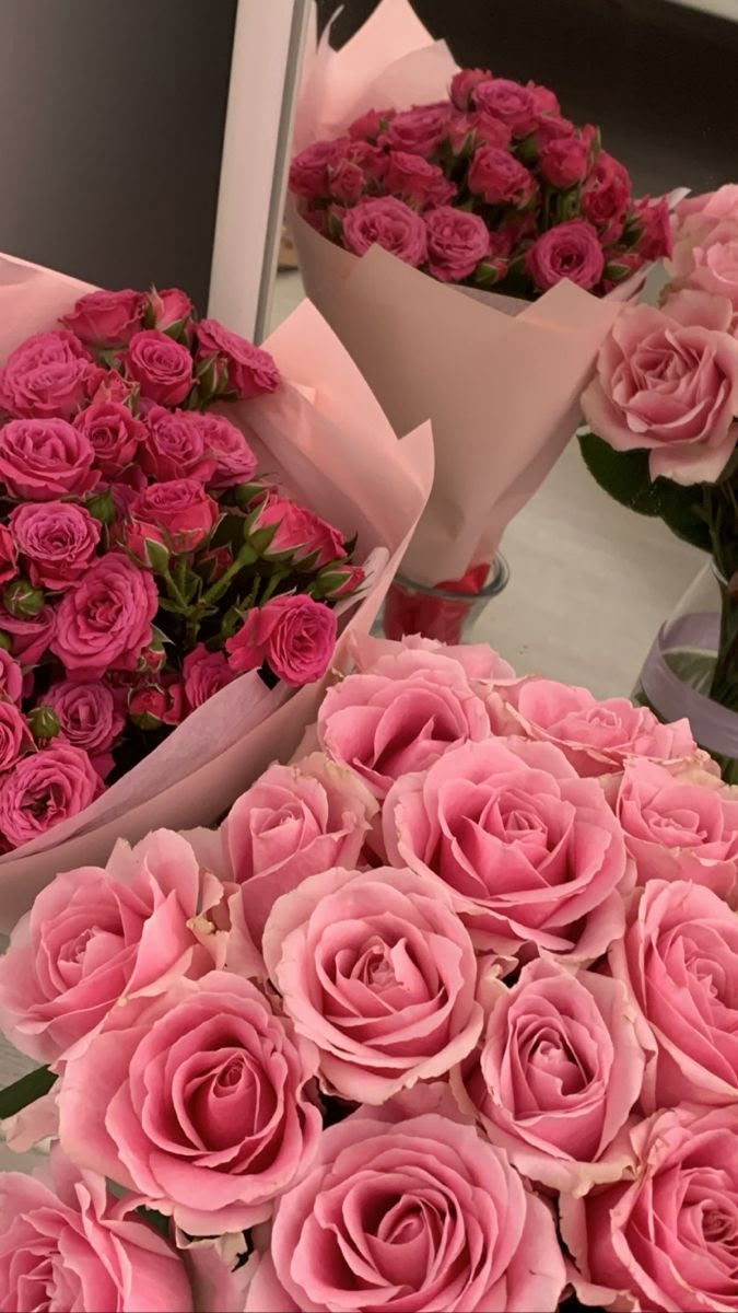 many pink roses are arranged on a table with the reflection of another person in the mirror