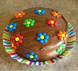 a cake with chocolate frosting and colorful flowers on the top is sitting on a plate