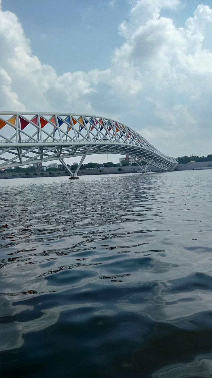 a long bridge over the water with flags on it's sides and some clouds in the background