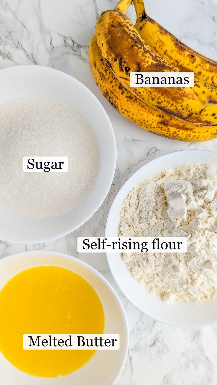 ingredients to make banana muffins in bowls on a marble counter top with bananas