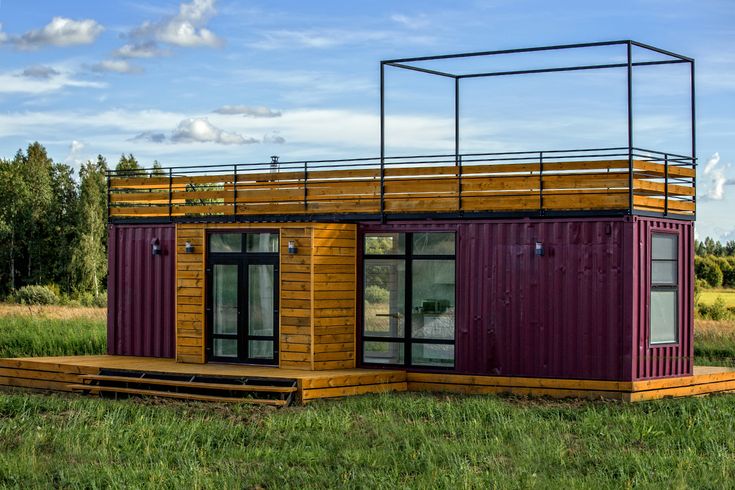 a small house made out of shipping containers in the middle of a field with grass and trees