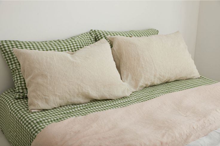 a bed with two pillows on top of it next to a white and green checkered comforter