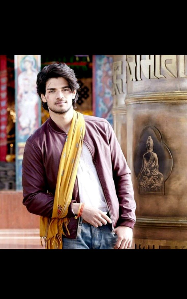 a man standing in front of a statue wearing a brown jacket and yellow scarf around his neck