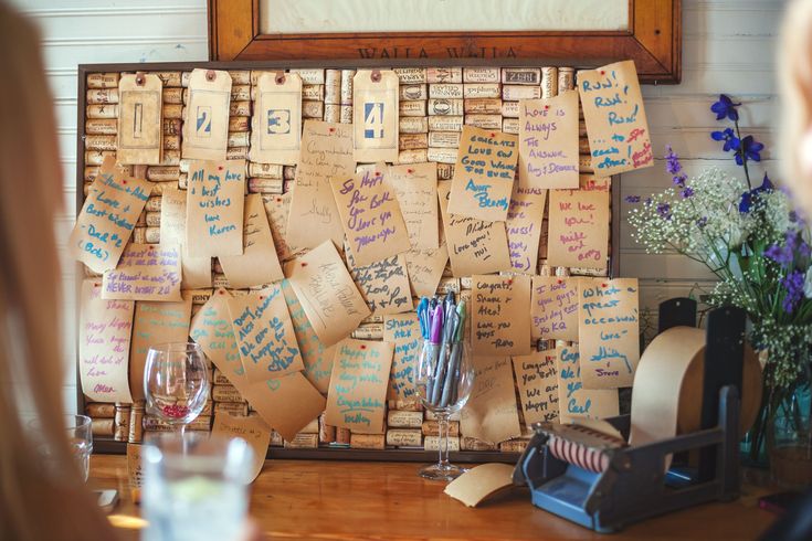 a cork board covered in lots of notes and writing on it's sides next to a vase filled with flowers