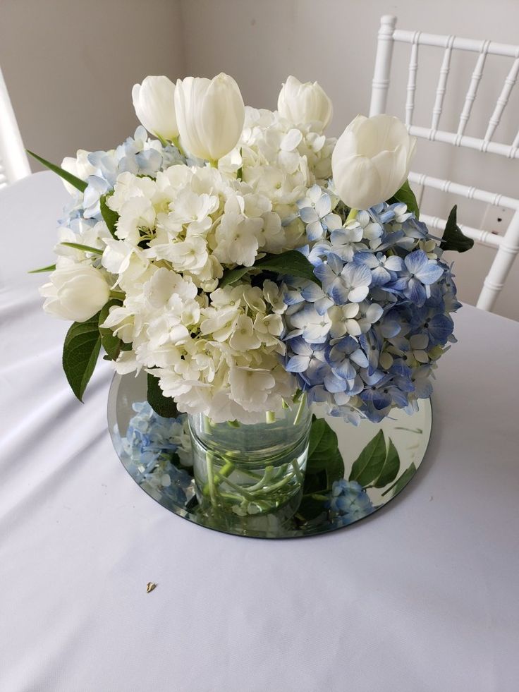 a vase filled with white and blue flowers on top of a table next to a chair