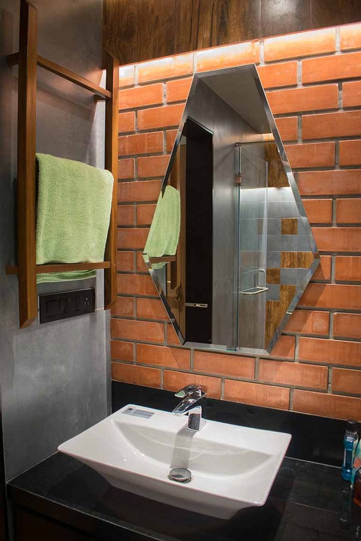 a bathroom sink sitting under a mirror in front of a brick wall with towels hanging on it