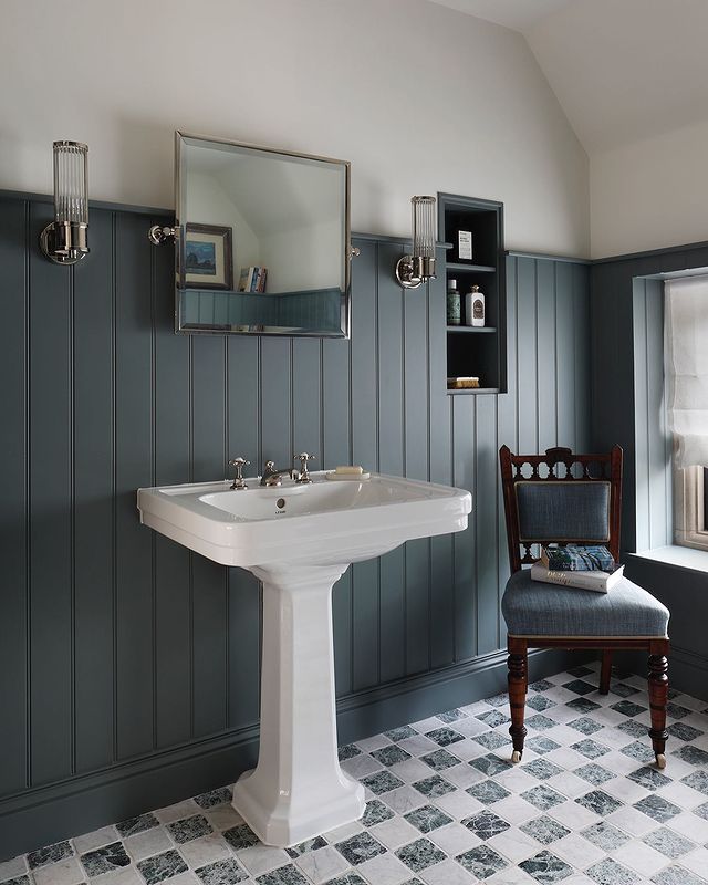 a white pedestal sink sitting under a mirror in a bathroom next to a wooden chair