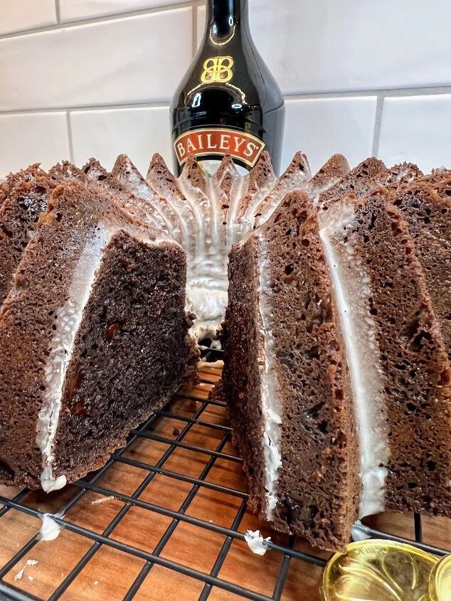 a chocolate bundt cake with frosting on a cooling rack next to a bottle of bailey's