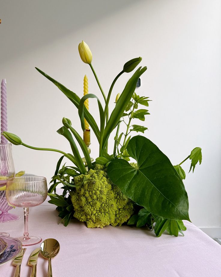 an arrangement of flowers and greenery on a pink table cloth with gold cutlery