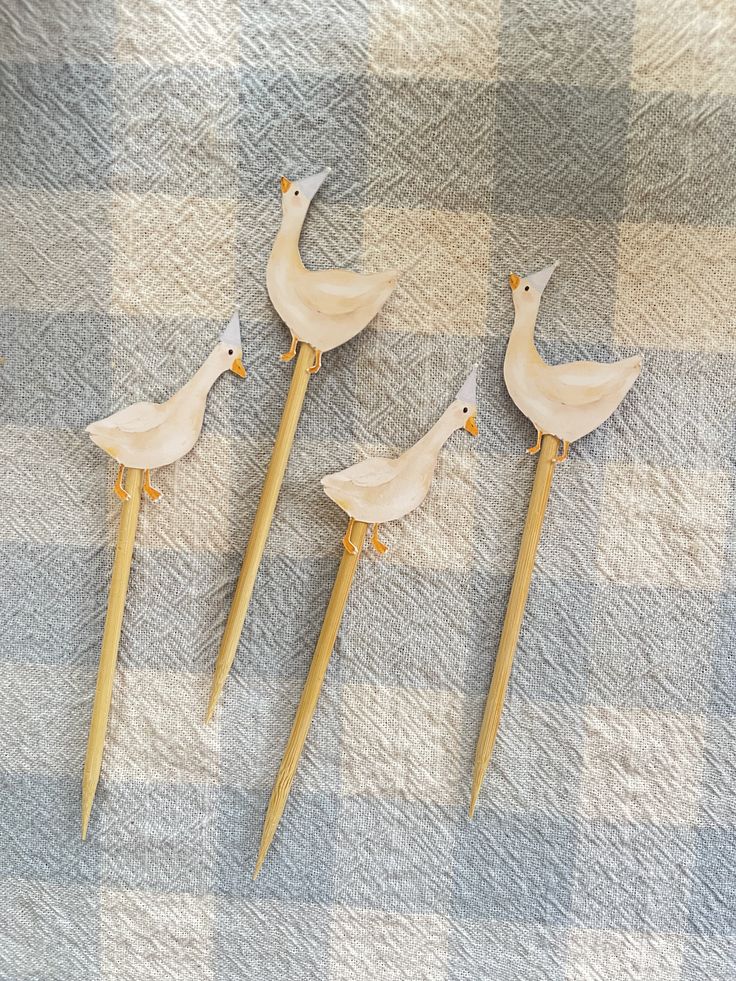 three wooden birds sitting on top of a checkered table cloth with long sticks sticking out of them