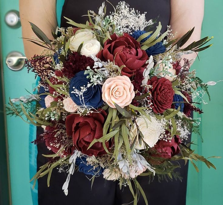 a woman holding a bouquet of red, white and blue flowers in front of a green door