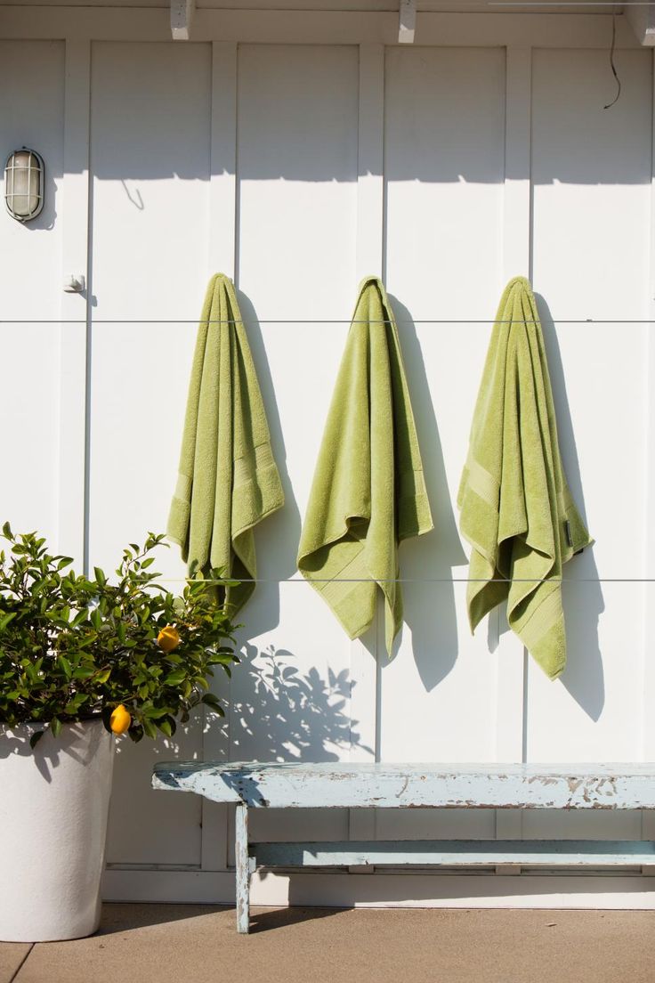 three green towels hanging on the side of a white wall next to a potted plant