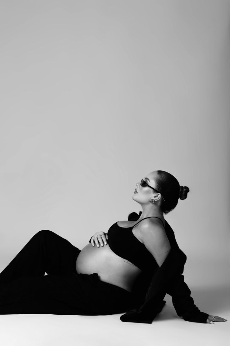 a pregnant woman sitting on the floor in black and white with her arms around her body