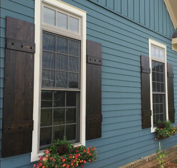 two windows with wooden shutters and flower boxes on the side of a blue house