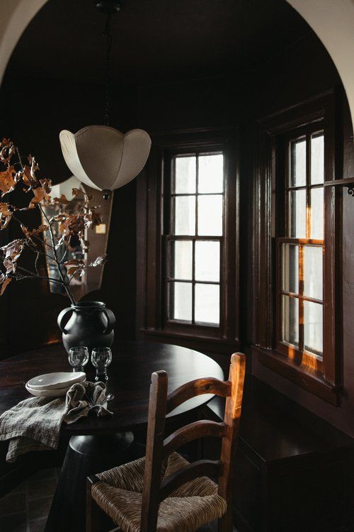 a dining room table with chairs and a vase on the table in front of two windows