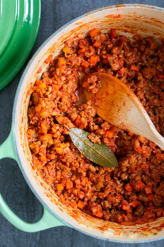 a wooden spoon in a pot filled with ground beef and carrots next to a green casserole dish