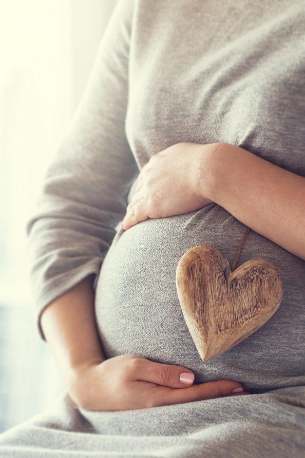 a pregnant woman holding a wooden heart in her belly