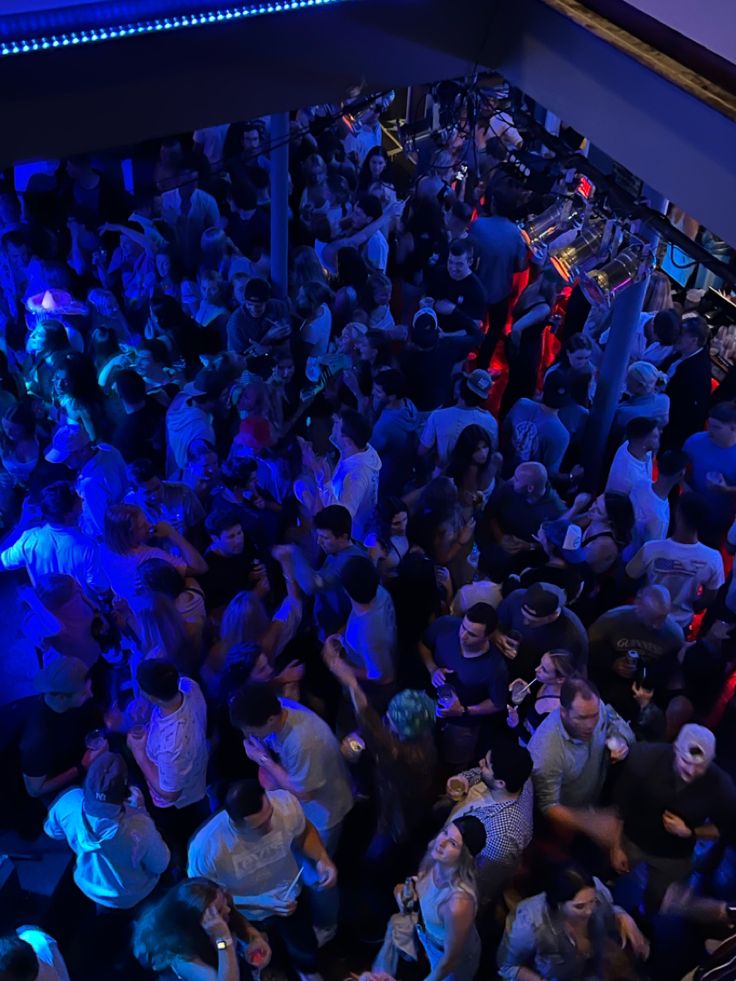 a large group of people standing around in a room with blue lights on the walls