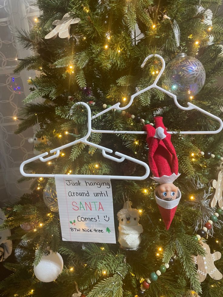 an elf hanging from a clothes hanger on top of a christmas tree