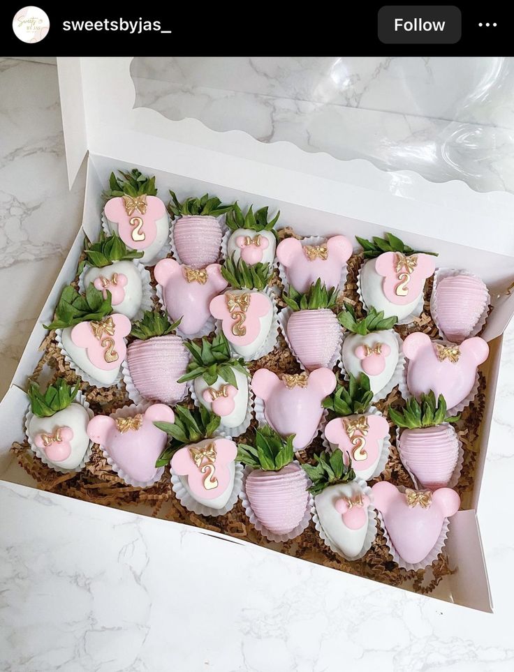 a box filled with lots of pink and white heart shaped cupcakes on top of green leaves