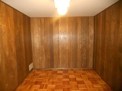 an empty room with wood paneling on the walls and wooden floors, in front of a light fixture