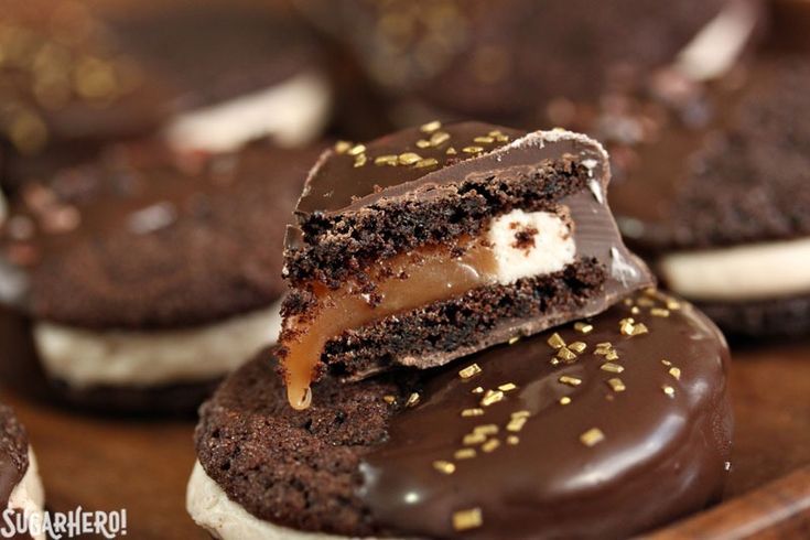 chocolate covered cookies with marshmallows are on a wooden tray and one is cut in half