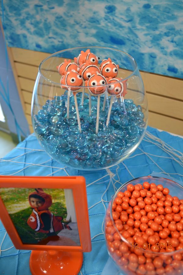 an orange and blue table topped with lots of candies next to a glass bowl filled with lollipops