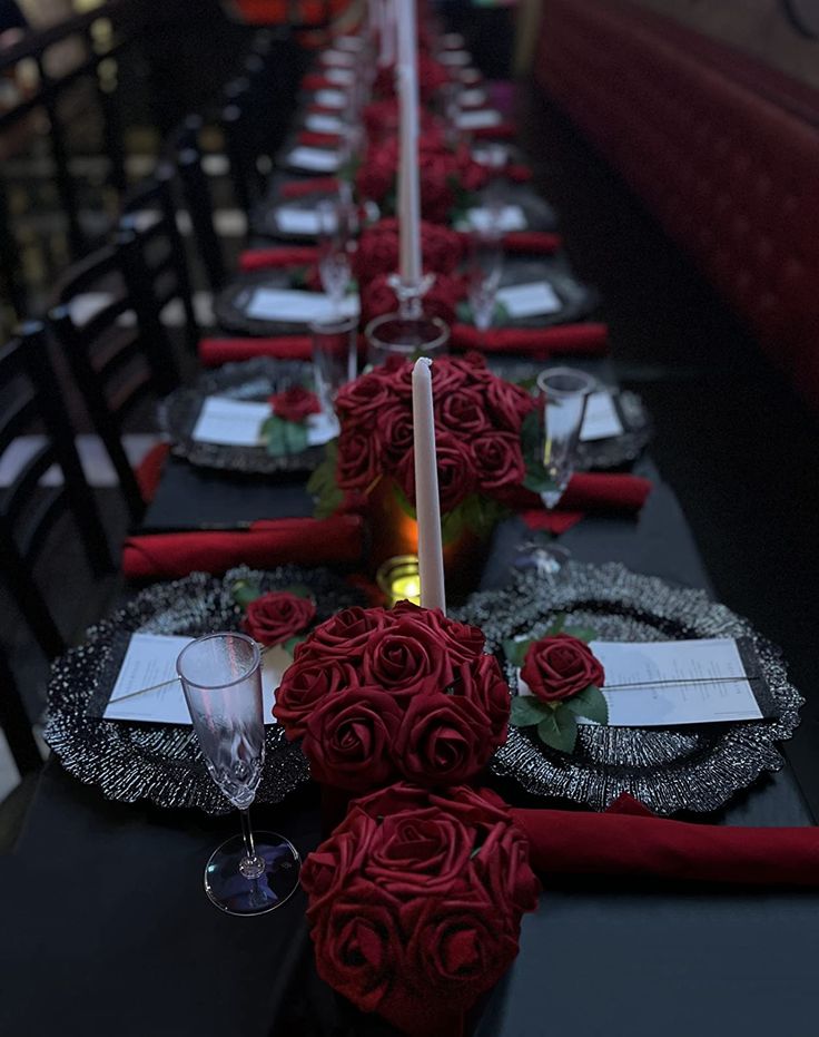 the table is set with red roses and place settings