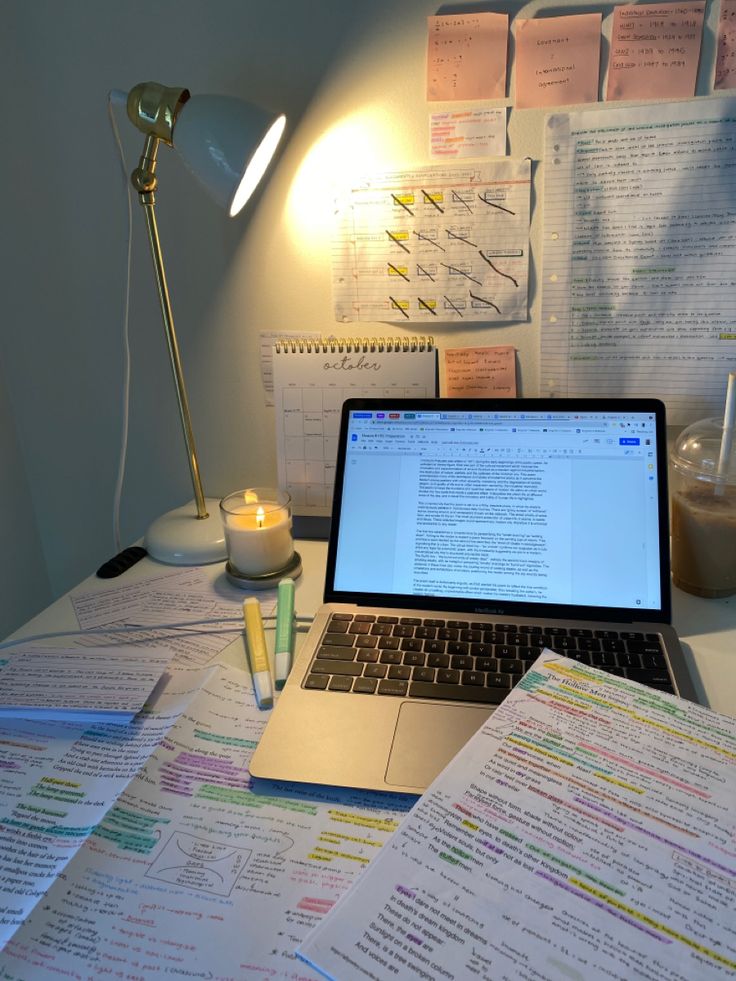 an open laptop computer sitting on top of a desk next to papers and a lamp