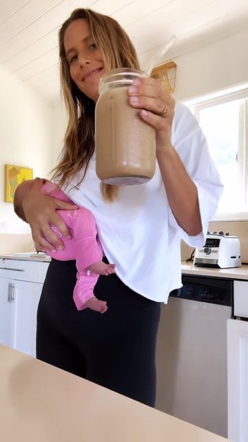 a woman holding a baby in her arms while holding a mason jar filled with liquid