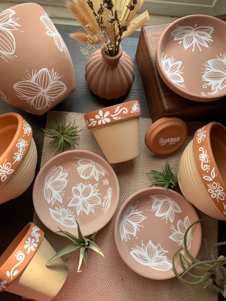 an assortment of ceramic dishes and vases with flowers painted on the side, sitting on a table