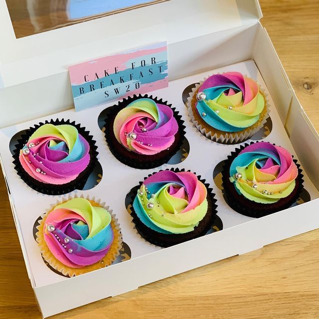 six cupcakes with colorful frosting in a white box on a wooden table