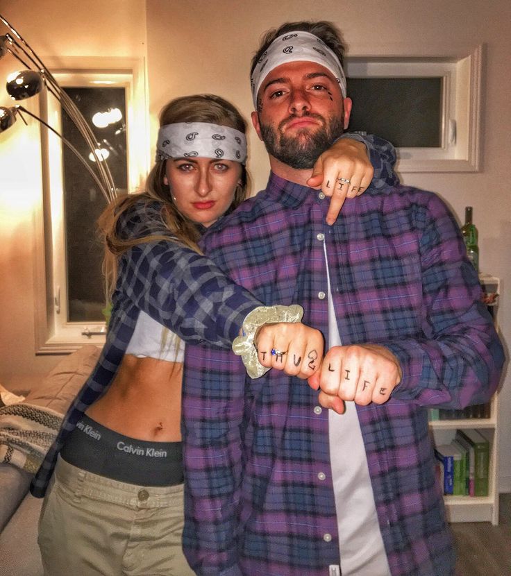 a man and woman standing next to each other in a living room with one pointing at the camera