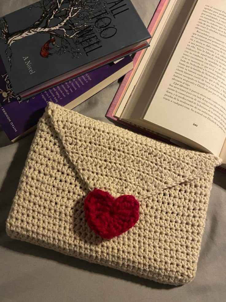 a crocheted bag with a red heart on it next to an open book