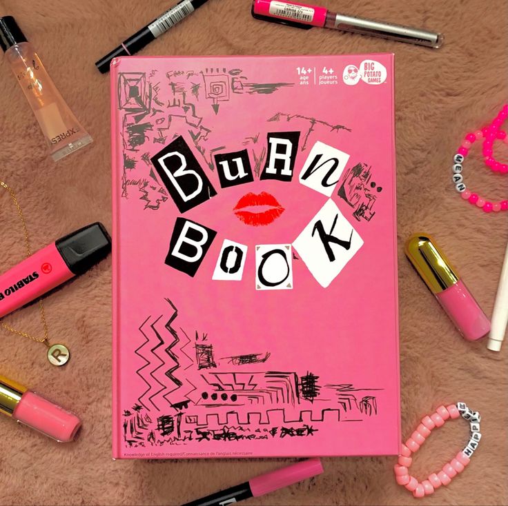 a pink book with the words burn book written on it surrounded by lipstick and other items