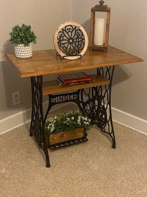 an antique sewing table with a plant on top and a candle next to it in a corner