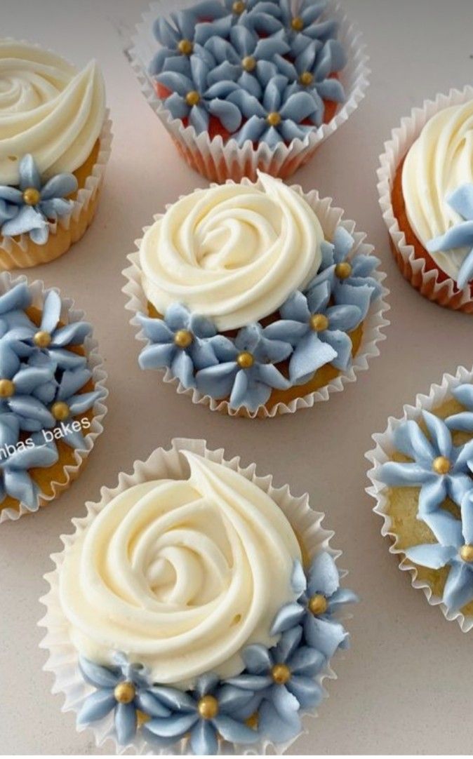 six cupcakes with white frosting and blue flowers