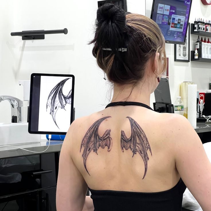 a woman with a bat tattoo on her back is sitting in front of a computer