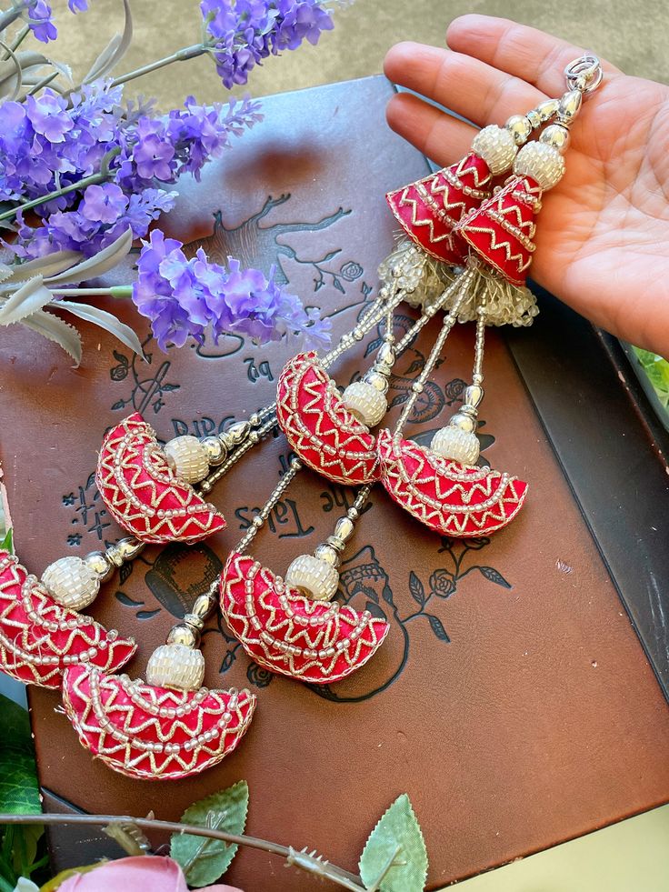 a hand is holding two red and white earrings on a book with flowers in the background