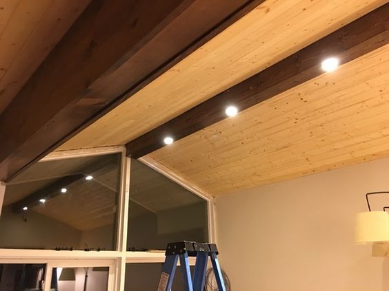 an unfinished room with wooden ceiling and ladders in the foreground, lights on