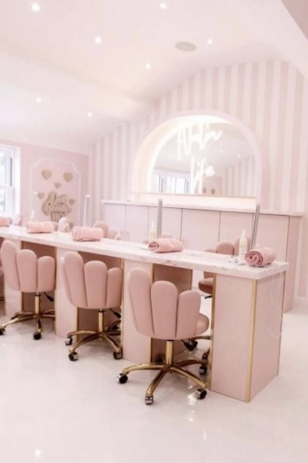 a pink and gold dining room with chairs, tables and chandelier in the background