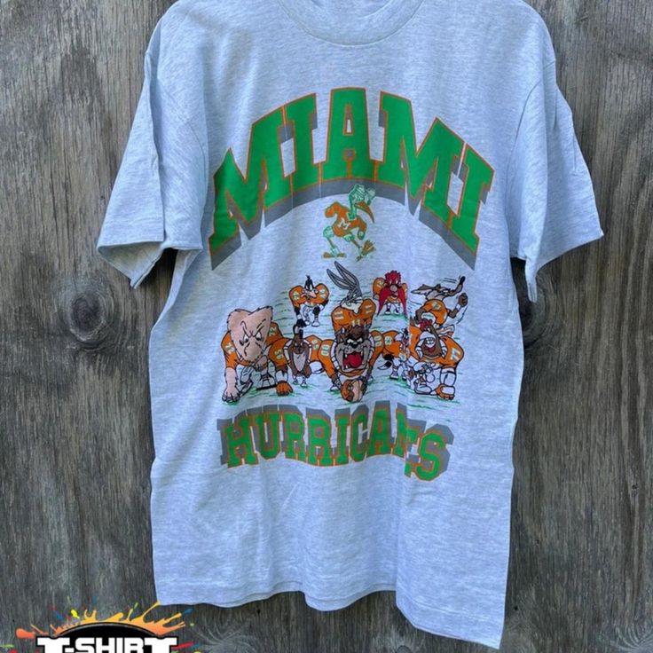 Vintage Ncaa Miami Hurricanes Looney Tunes T-Shirt, Miami Hurricanes Shirt, University Of Miami, Unisex T-Shirt Sweatshirt, Vintage Shirt Our Classic T-Shirt Serves As The Perfect Short-Sleeved Shirt For Your Unique, Funny, Or Personalized Designs. Brand: Gildan Heavy Weight Fabric Classic Unisex Makes This An Easy Fit Size Up If You Want Something Roomier Our Shirts Materials: 100% Cotton ** Note: - Double Check Your Address Before Ordering. - If You Want To Return The Goods, You Are The One To Gray Logo Print Top For Fan Merchandise, Casual Fan Apparel T-shirt With Graphic Print, Fan Gear Graphic Tee With Crew Neck, Graphic Tee Tops With Fan Gear Graphic Print, Casual Fan Gear Graphic T-shirt, Graphic Tee Tops With Graphic Print For Fans, Casual Graphic Print T-shirt For Fan Gear, Fan Gear Graphic Tee Shirt With Short Sleeves, Graphic Tee Shirt For Fan Gear With Short Sleeves