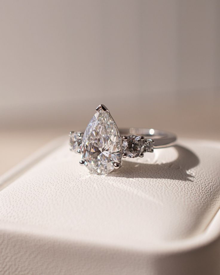 a three stone diamond ring sitting on top of a white box with its reflection in it