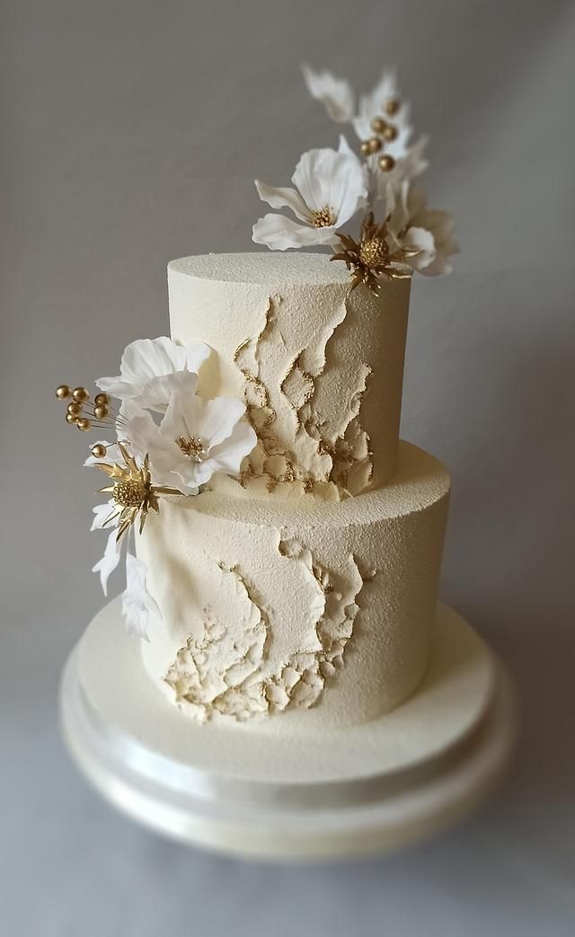 a three tiered cake with white flowers on it's side and gold accents