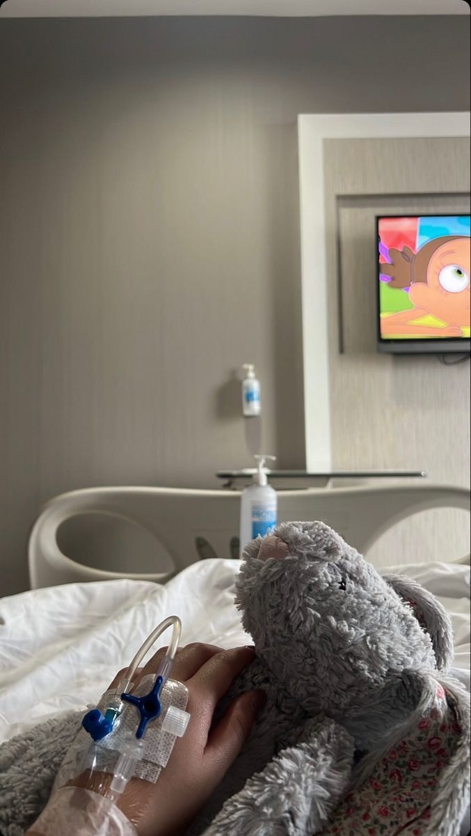 a person laying in a hospital bed with a stuffed animal and iv drip tube attached to their arm