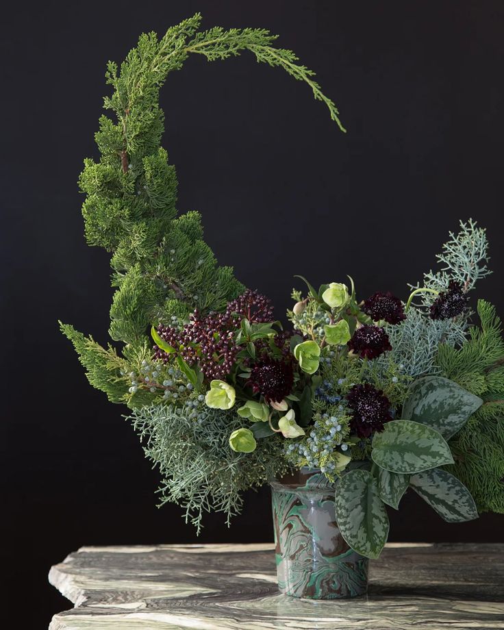 a vase filled with flowers and greenery on top of a table