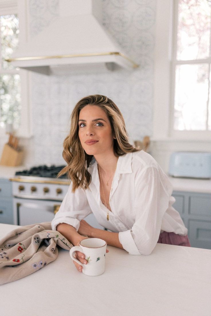 a woman sitting at a kitchen counter with a mug in her hand and looking off to the side