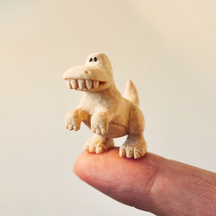 a small toy dinosaur sitting on top of someone's finger with its mouth open