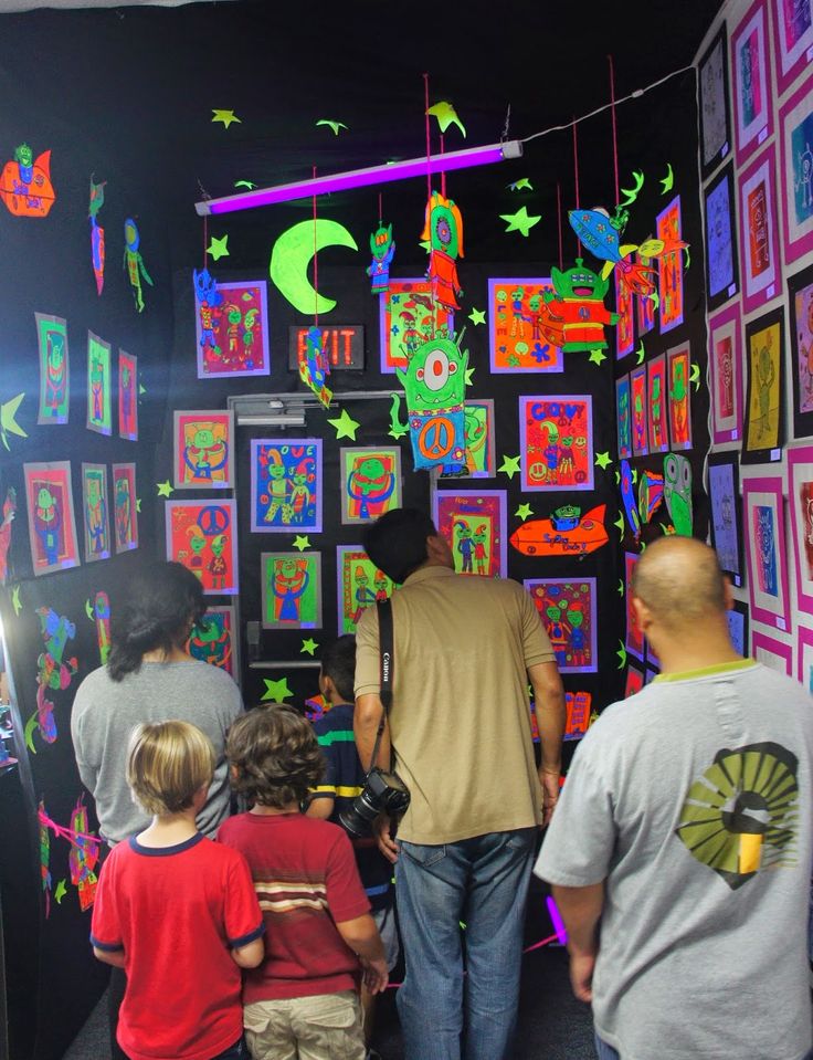 a group of people standing in front of a wall with pictures on it and hanging from the ceiling